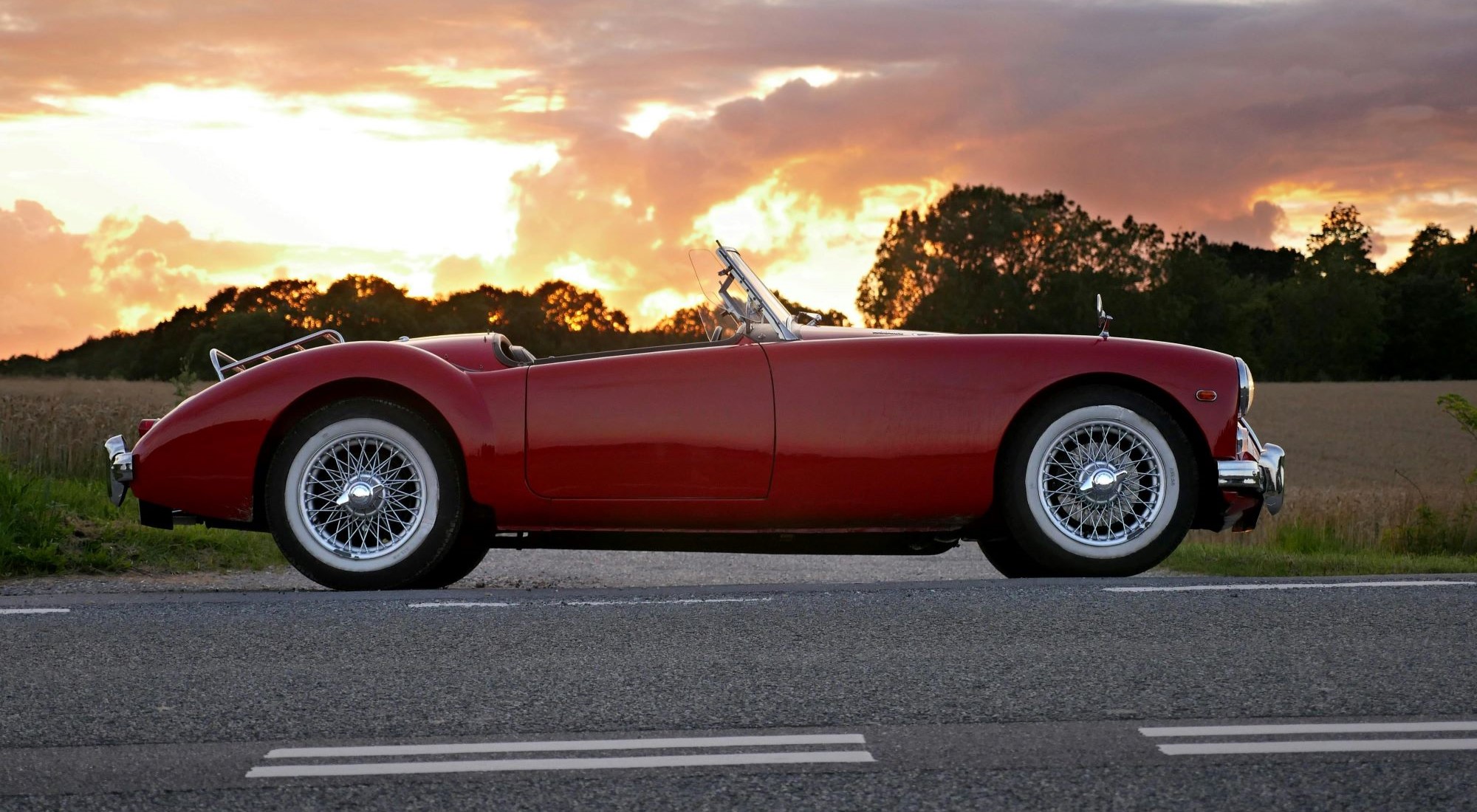 ein Bild, das ein rotes Cabriolet auf der Straße im Sonnenuntergang zeigt