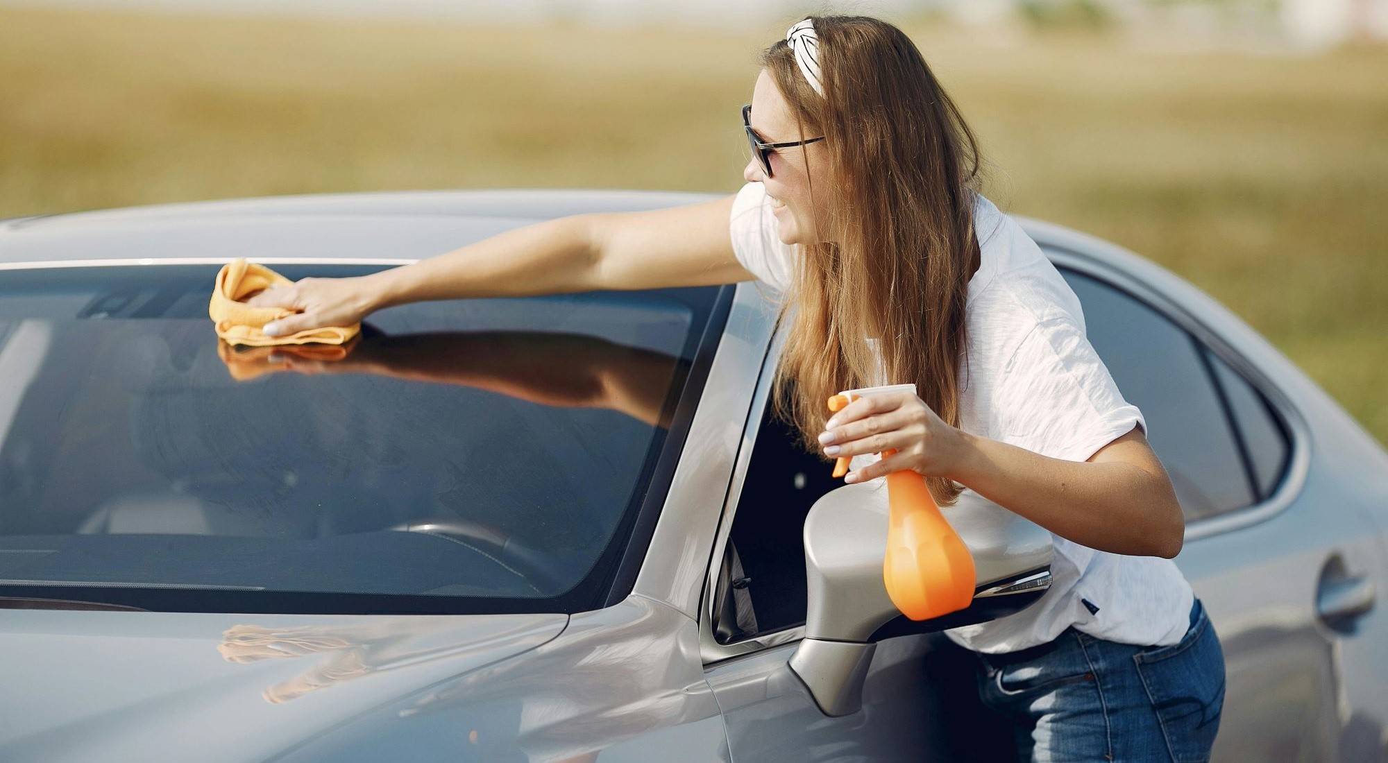 Frau reinigt Autoscheibe mit Lappen und Sprühflasche